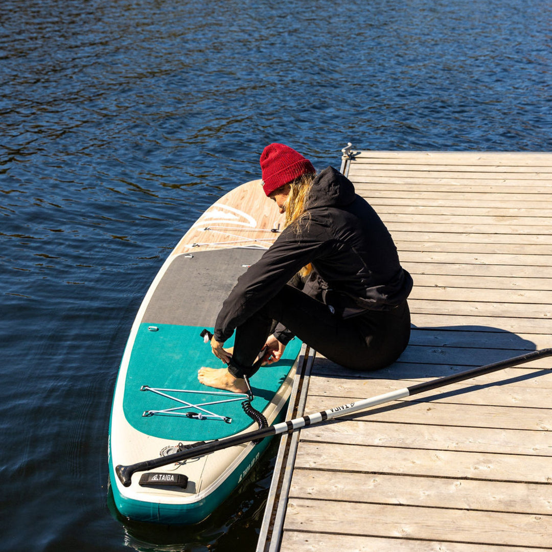 Person attaching leash to paddle board wearing red beanie