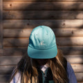 Person wearing a teal cap with a logo against a wooden wall