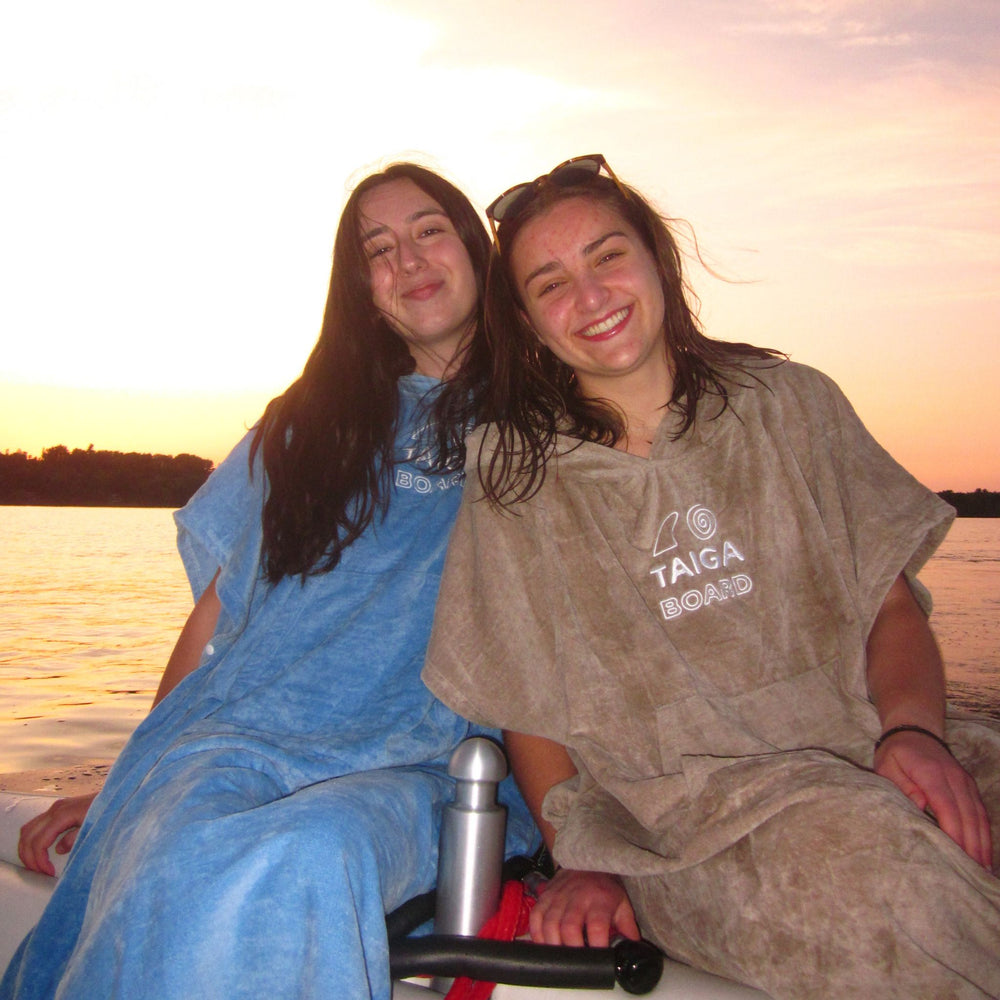 Two women sitting together on a boat at sunset, wearing matching lounge ponchos.