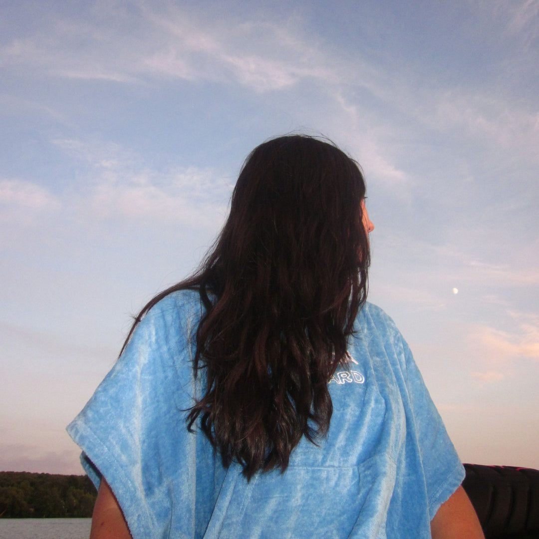 A person with long dark hair seen from behind, wearing a light blue poncho towel