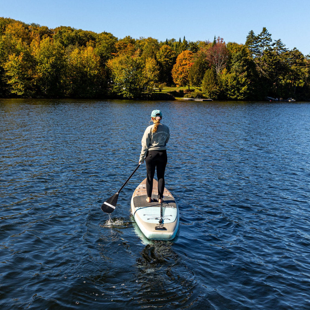 Person standing on a paddleboard, wearing a crewneck with 'Slow Rider Club' text.