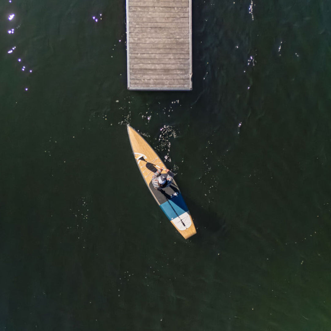 Aerial view of a person paddling a SUP near a wooden dock on a lake.
