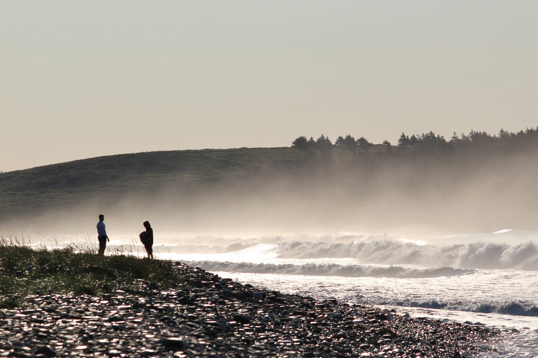 Two people standing on a beach with waves crashing in the background