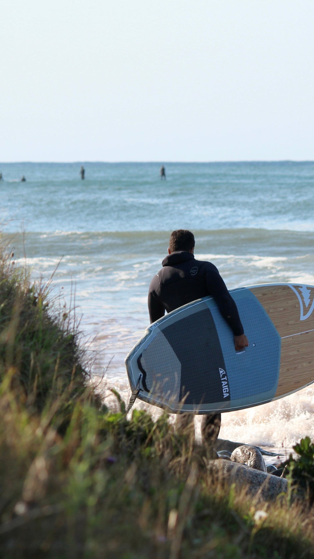 Person holding our El Niño SUP Surf on a beach with waves in the background