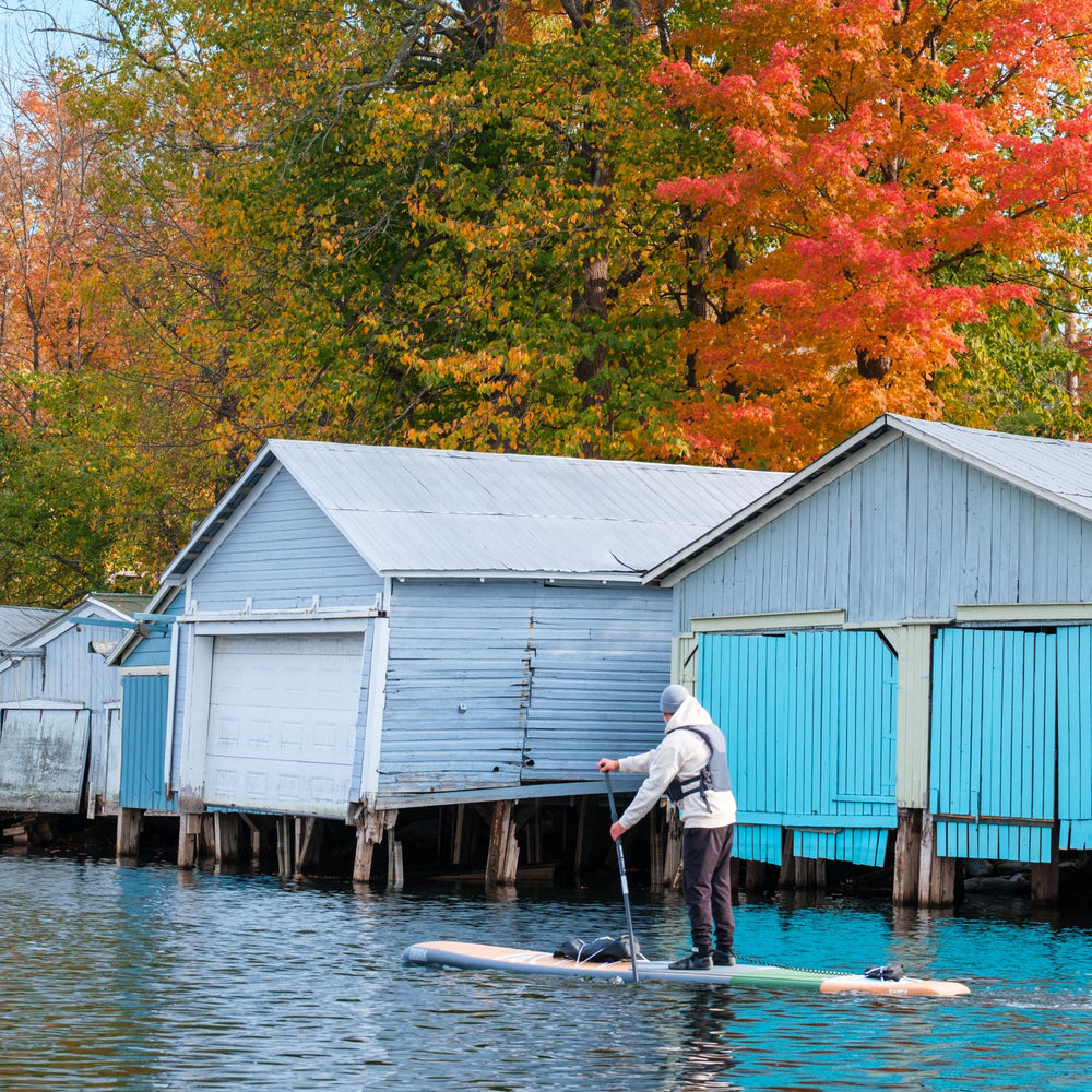 Paddler on a hard wooden SUP near boat houses in fall