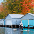 Paddler on a hard wooden SUP near boat houses in fall
