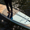 Person standing on a paddleboard with a leash attached, on a body of water.