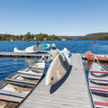 Person with a paddleboard on a dock by a lake with other boats and a clear sky.