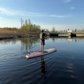 Person paddleboarding on a calm lake with a bridge and trees in the background