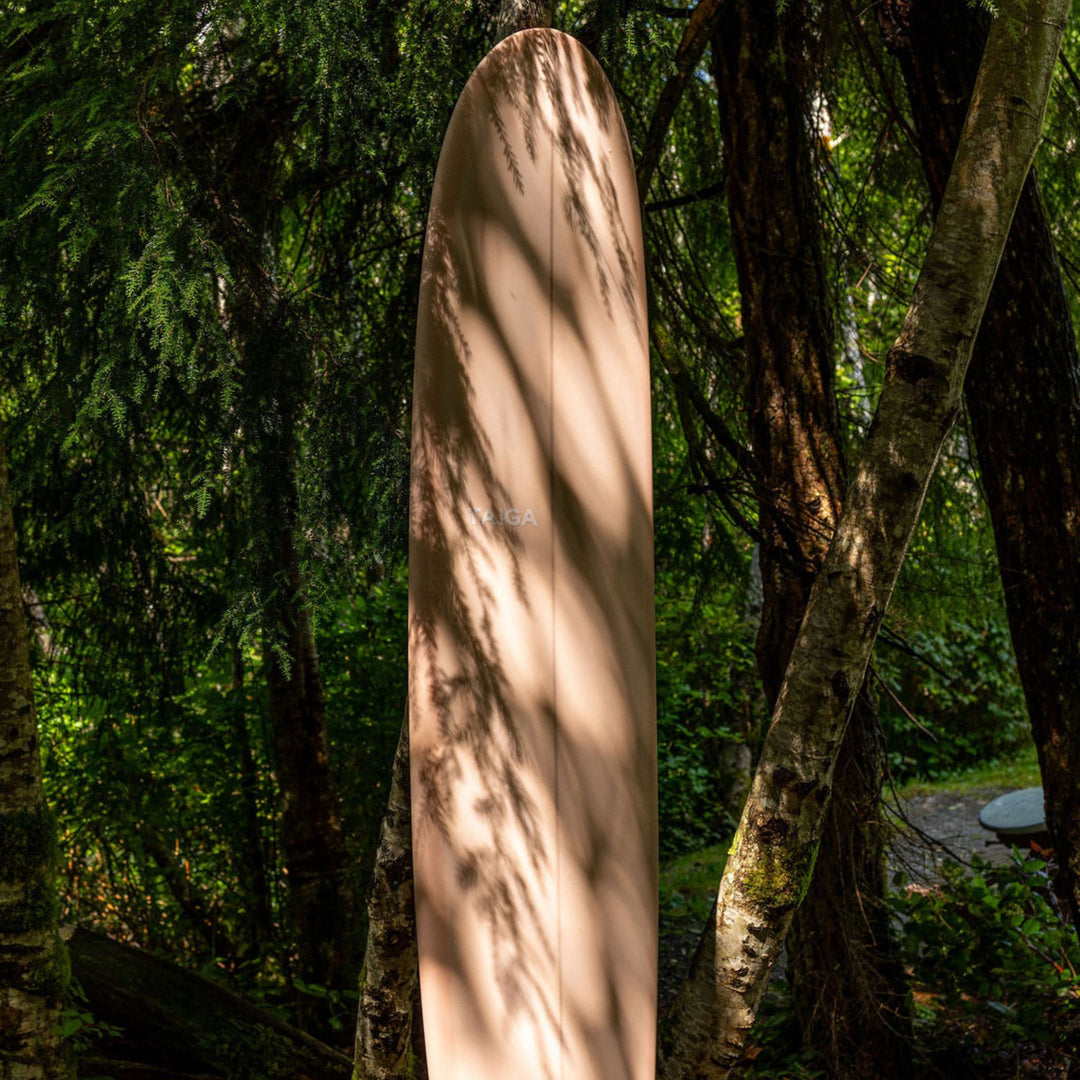Front View of The Longboard Surf Board in The Rosé Color In The Forest