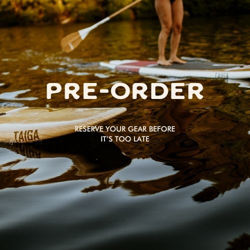 A calm lake scene with a paddleboard visible in the background and large overlaid text reading 'PRE-ORDER' plus smaller text 'RESERVE YOUR GEAR BEFORE IT'S TOO LATE.' A Taiga paddleboard is partially visible in the foreground, and part of a person standing on a paddleboard is shown at the top right.