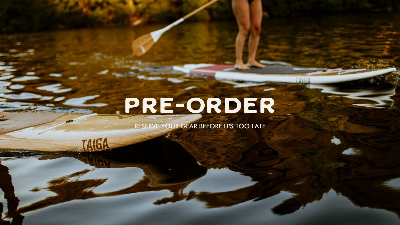 A stand-up paddleboard scene on calm water with a person standing on a paddleboard in the background and another board in the foreground. Large overlaid text reads 'PRE-ORDER' with smaller text below, and the brand name 'TAIGA' is visible on the paddleboard.