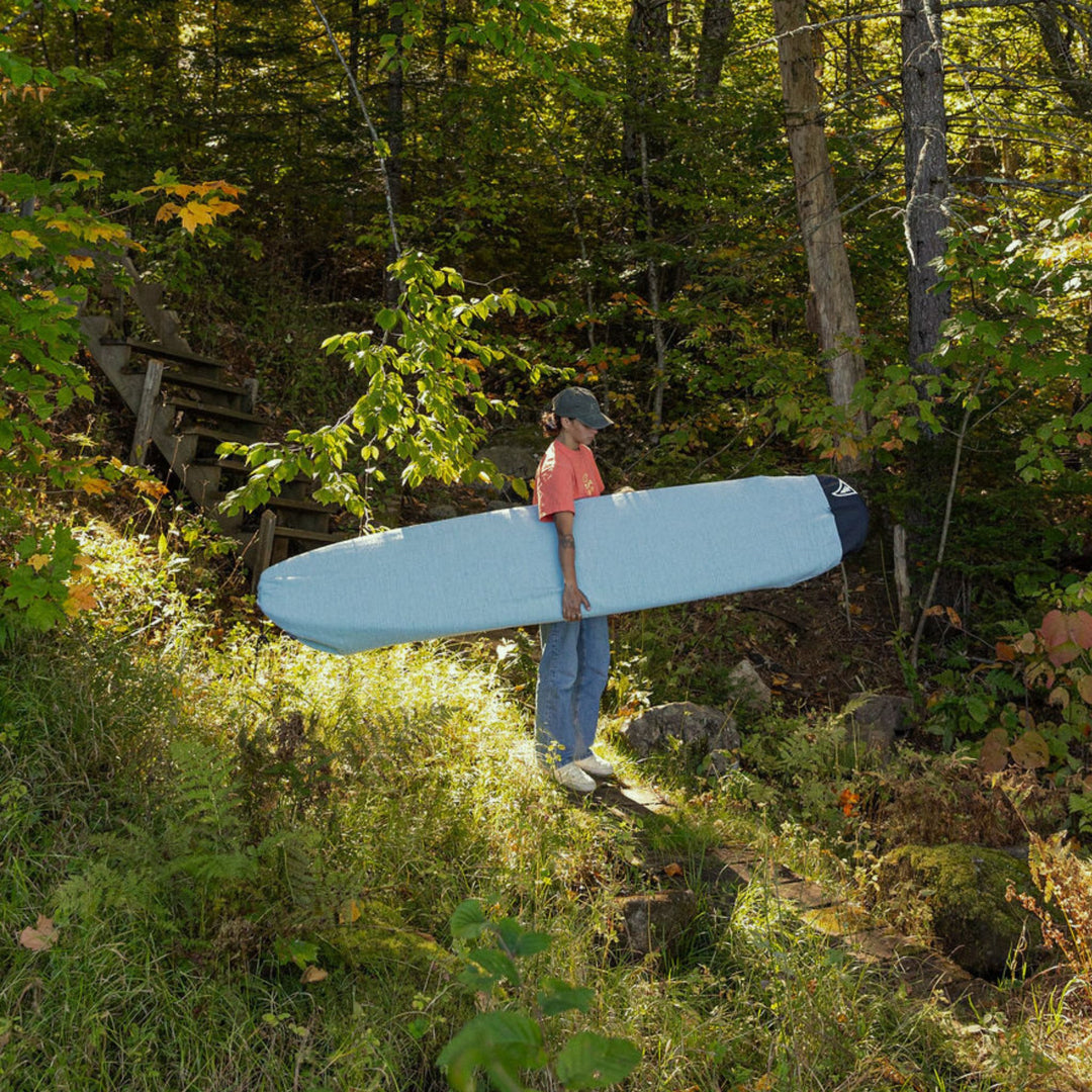 Person carrying a surfboard through a forest
