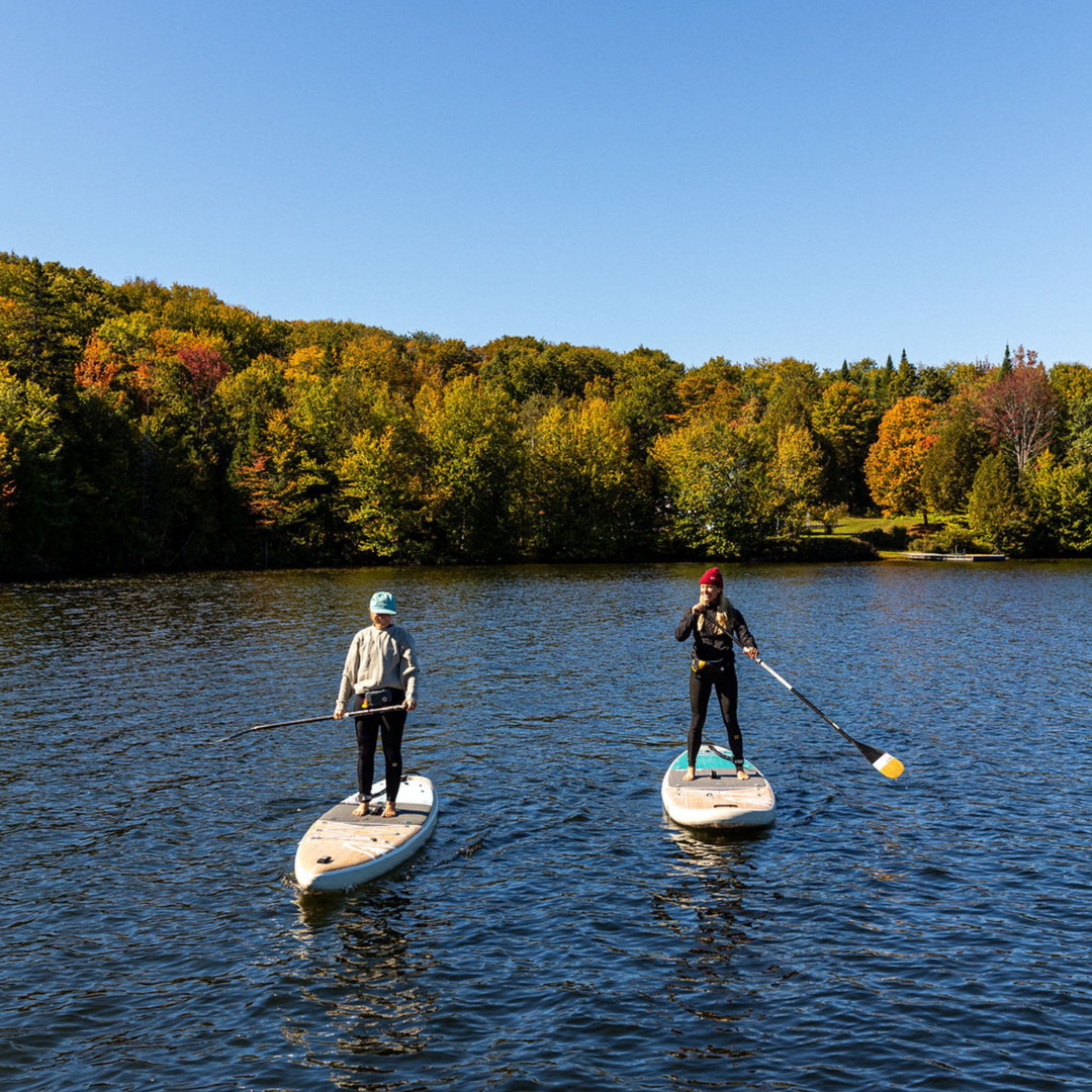 Two people paddleboarding on a lake with autumn foliage in the background