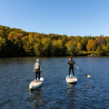 Two people paddleboarding on a lake with autumn foliage in the background
