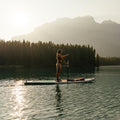 Person paddleboarding on a lake with mountains and trees in the background