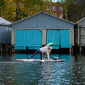 Girl doing yoga on a on a hard wooden SUP near boat houses in fall