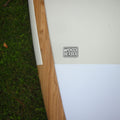 Close-up of a white textured outdoor furniture pad or cushion with a visible 'WOOD SERIES' logo, bordered by a natural wood frame, placed outdoors next to green grass.