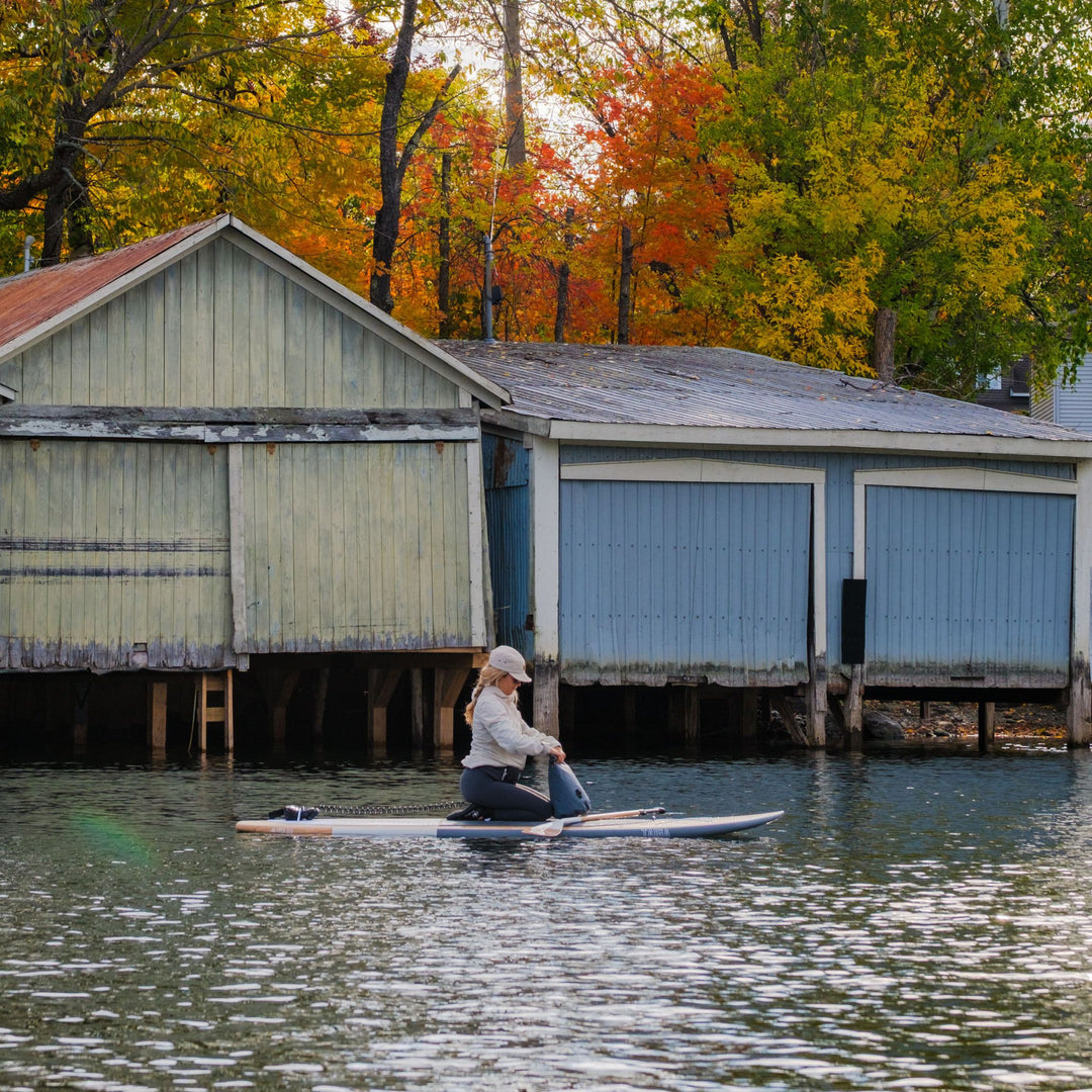 Paddler on a hard wooden SUP near boat houses in fall
