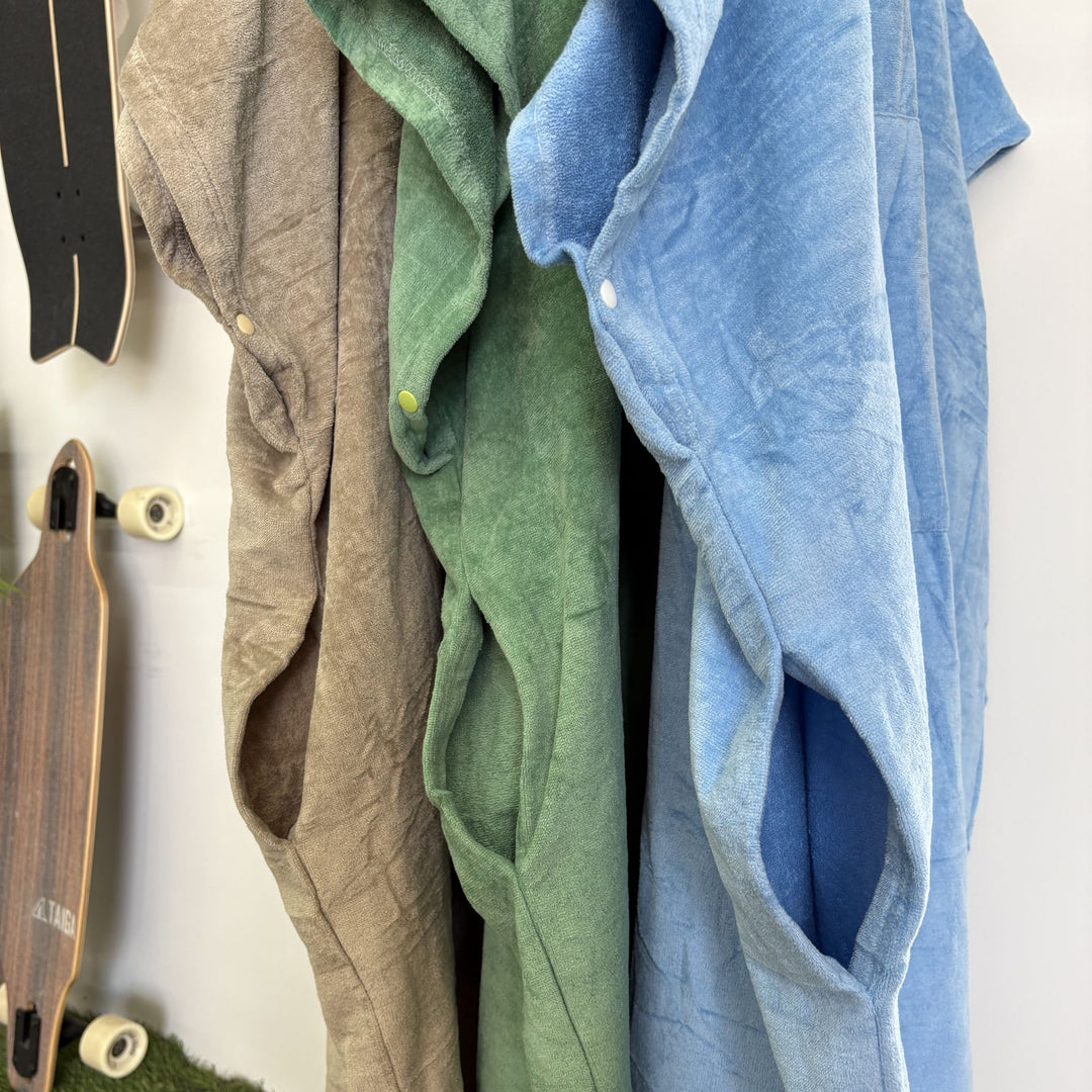 Three ponchos slits in different colors hanging on a wall with two skateboards below.