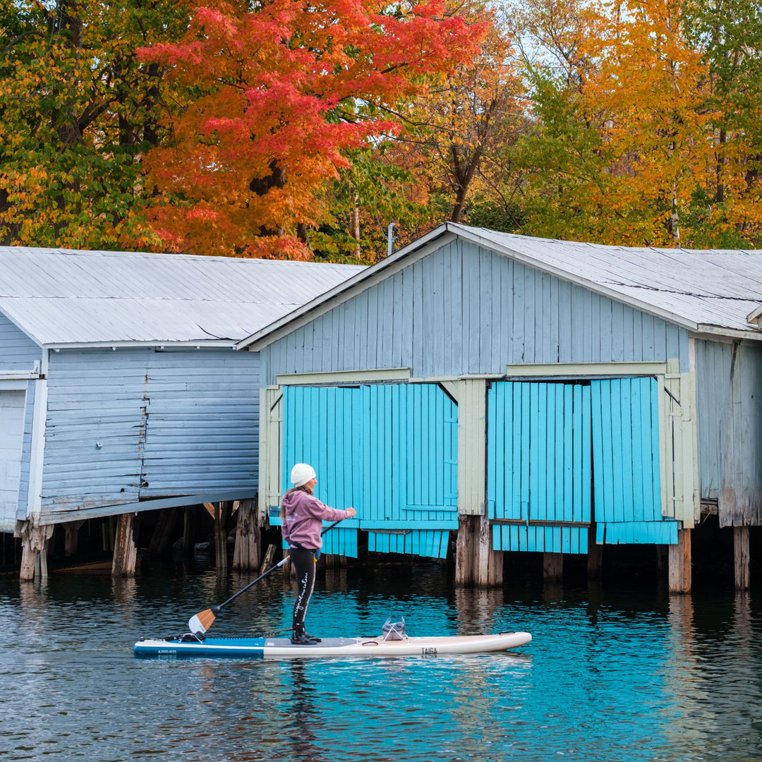 Paddler on an inflatable SUP near boat houses in fall