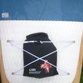 A black Taiga nautical safety kit pouch with white cords and metal clips, laid flat on a white textured pad with a blue Wood Series board visible underneath.
