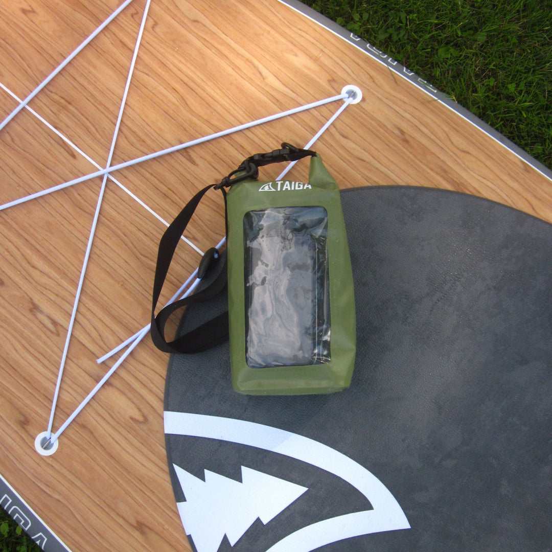 An olive green Taiga waterproof phone pouch with a clear front window and black strap, resting on a wooden board outdoors.