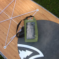 An olive green Taiga waterproof phone pouch with a clear front window and black strap, resting on a wooden board outdoors.