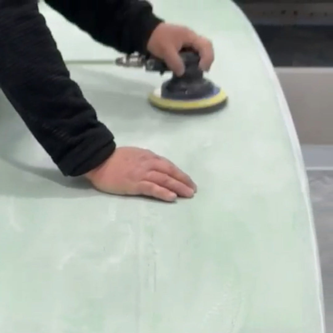 Person using a sanding machine on a surfboard