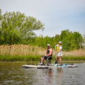 Two people on a paddleboard with one in a wheelchair, surrounded by trees and reeds.