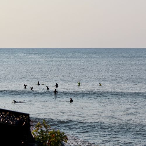People swimming in a large body of water with a building and trees in the foreground.