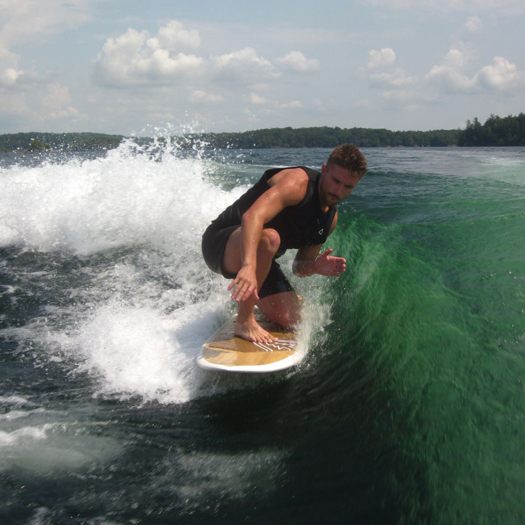 A man crouches on a WAKESURF riding a green wake wave in the water under a cloudy sky.